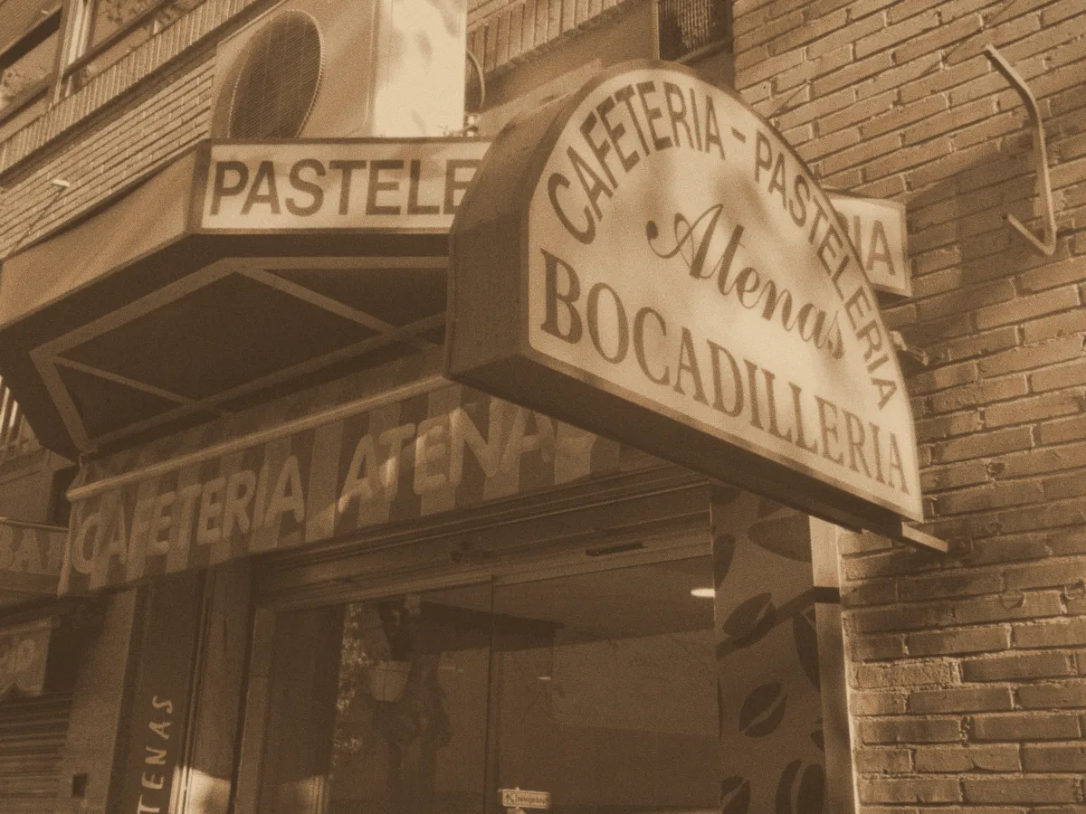 Fachada de la cafetería con el rótulo de Cafetería Pastelería Atenas Bocadillería, en sepia