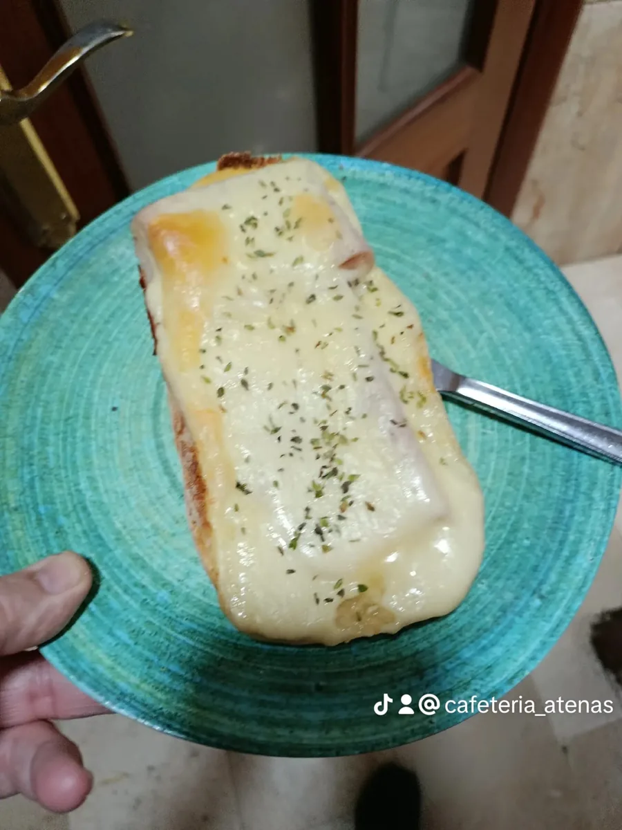 Tostada gratinada con jamón y queso fundido con orégano, en plato turquesa